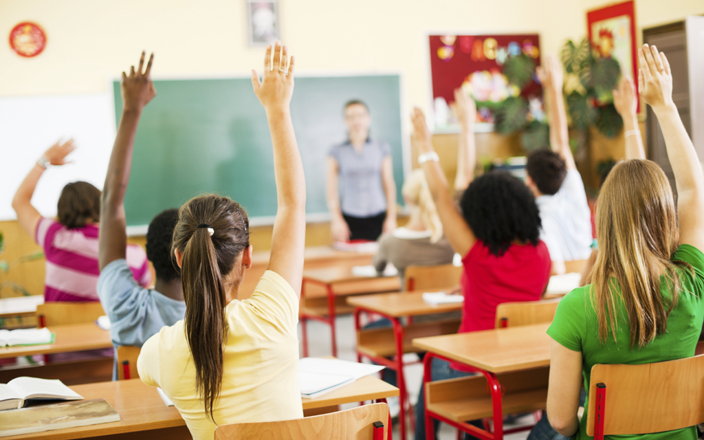 Alunos em sala de aula levantando a mão 